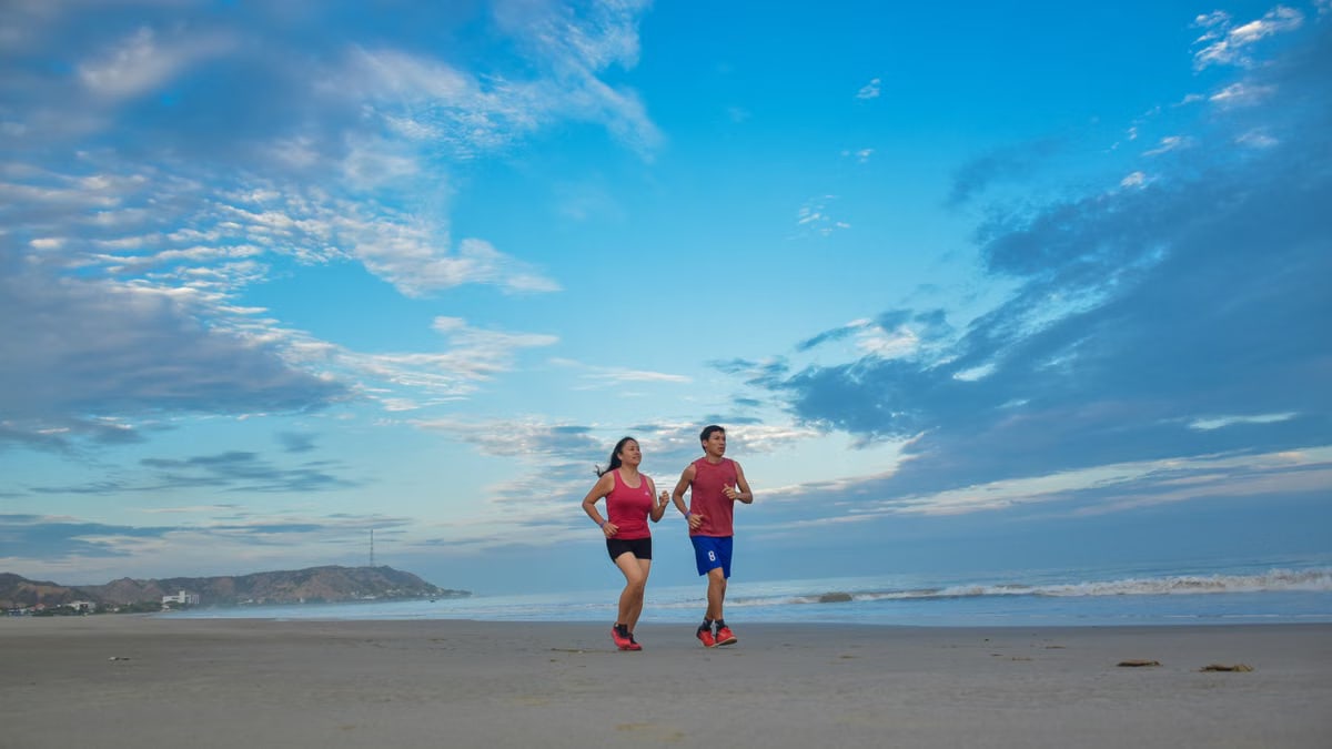 A couple enjoys jogging together along a scenic beach under a bright blue sky.